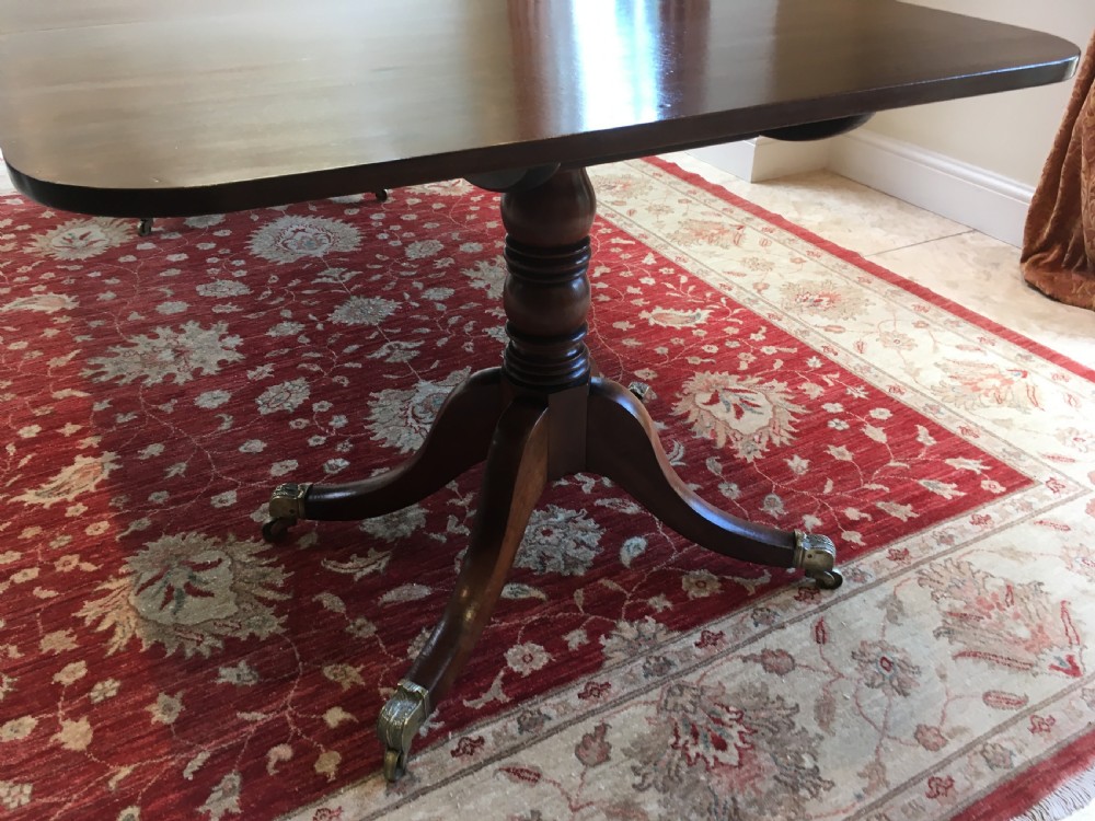A 19th-century mahogany extendable dining table featuring a polished rectangular top with rounded corners, supported by two turned pillar pedestals on splayed legs with brass castors. View VII