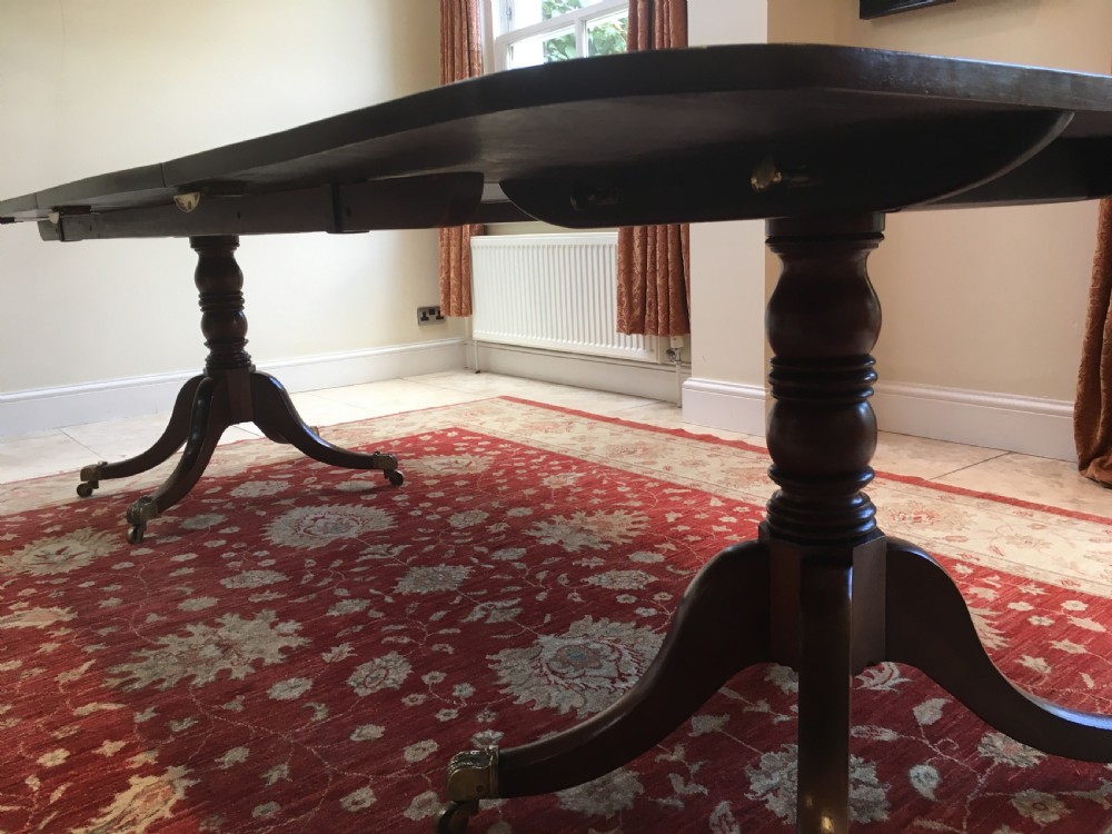 A 19th-century mahogany extendable dining table featuring a polished rectangular top with rounded corners, supported by two turned pillar pedestals on splayed legs with brass castors. View VIII