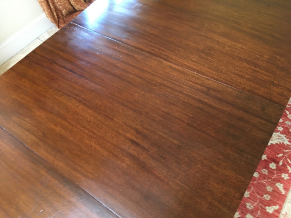 A 19th-century mahogany extendable dining table featuring a polished rectangular top with rounded corners, supported by two turned pillar pedestals on splayed legs with brass castors. View X