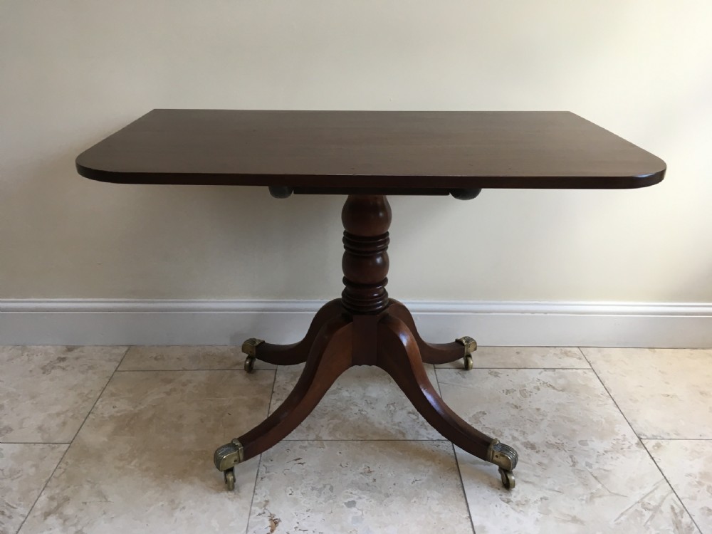 A 19th-century mahogany extendable dining table featuring a polished rectangular top with rounded corners, supported by two turned pillar pedestals on splayed legs with brass castors. View XV