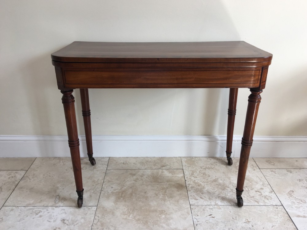 A Regency mahogany fold-over card table featuring turned tapered legs, brass castors, and boxwood stringing inlay along the frieze.