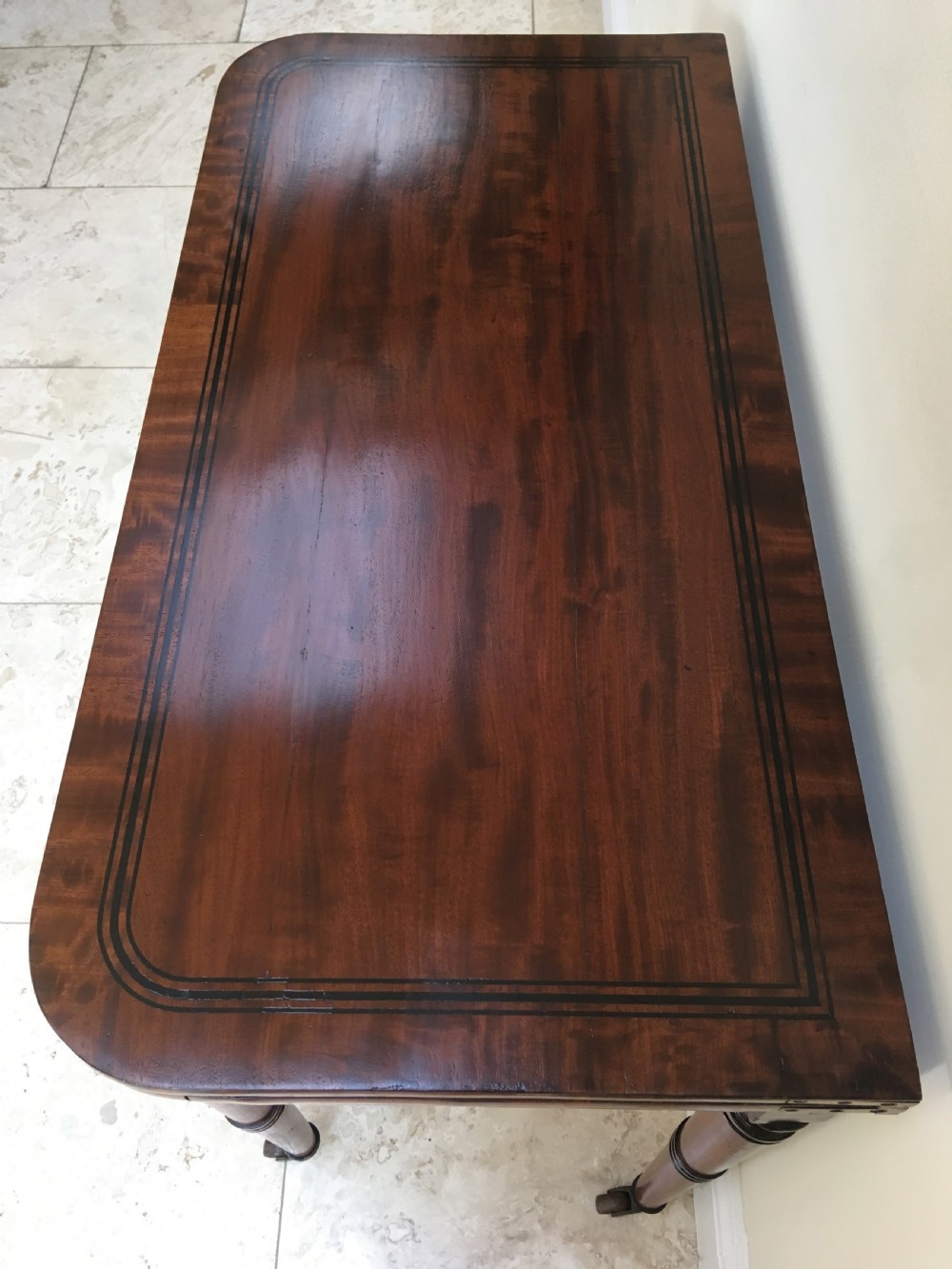 A Regency mahogany fold-over card table featuring turned tapered legs, brass castors, and boxwood stringing inlay along the frieze. View II