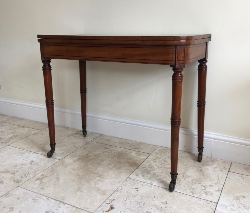 A Regency mahogany fold-over card table featuring turned tapered legs, brass castors, and boxwood stringing inlay along the frieze. View VI