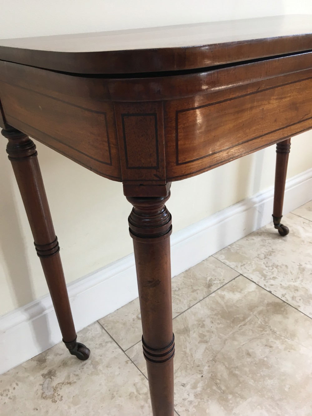 A Regency mahogany fold-over card table featuring turned tapered legs, brass castors, and boxwood stringing inlay along the frieze. View VII