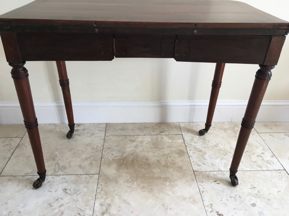 A Regency mahogany fold-over card table featuring turned tapered legs, brass castors, and boxwood stringing inlay along the frieze. View IX