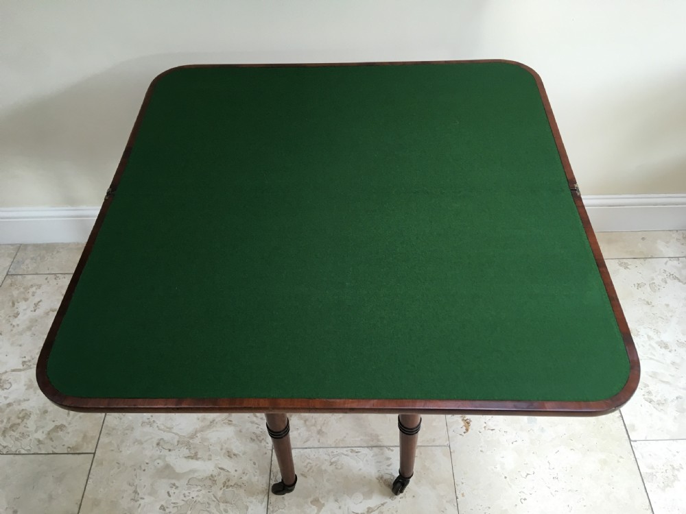 A Regency mahogany fold-over card table featuring turned tapered legs, brass castors, and boxwood stringing inlay along the frieze. View X