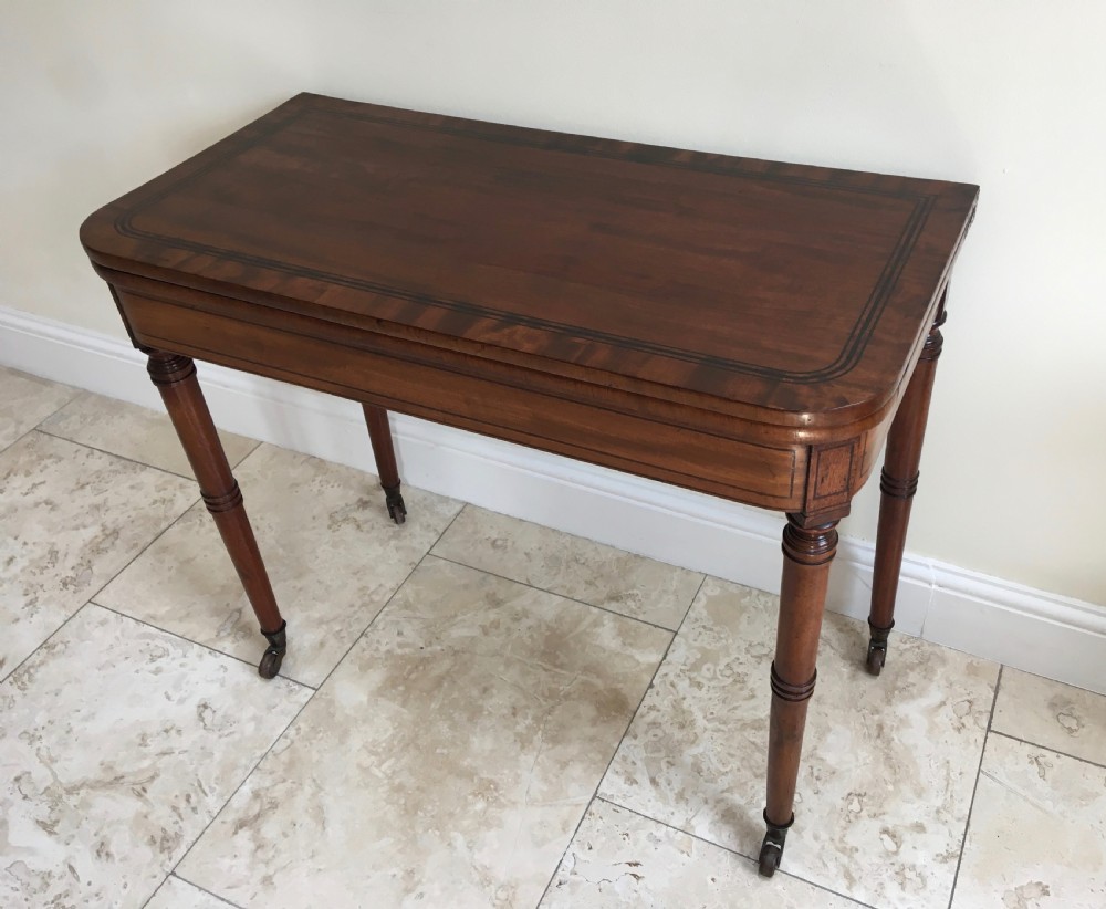 A Regency mahogany fold-over card table featuring turned tapered legs, brass castors, and boxwood stringing inlay along the frieze. View XI