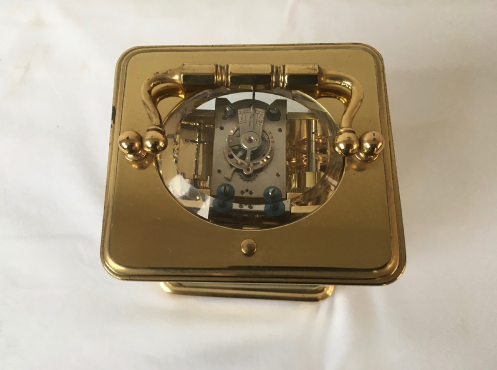 A rectangular brass carriage clock featuring clear bevelled glass panels, a white enamel dial with Roman numerals, a subsidiary alarm dial, and decorative corner finials. View VIII