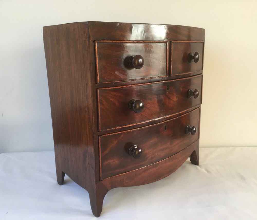 A miniature mahogany bow-fronted chest of drawers featuring turned wooden knobs and a polished grain finish.