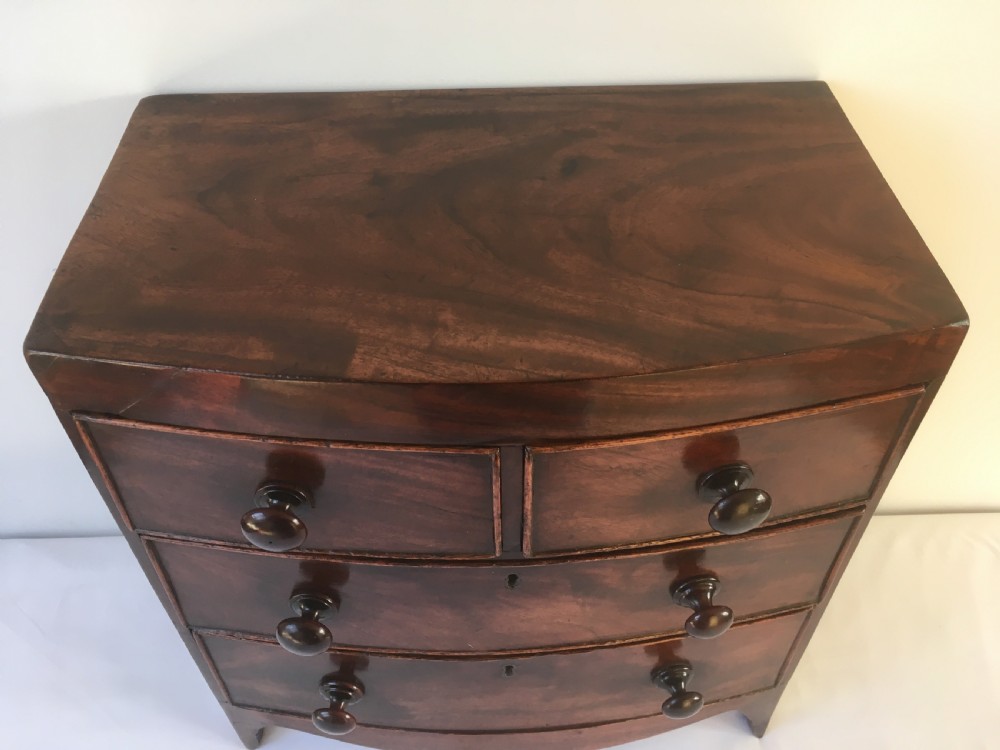 A miniature mahogany bow-fronted chest of drawers featuring turned wooden knobs and a polished grain finish. View II