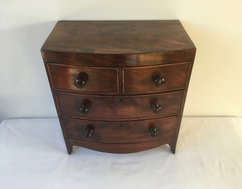 A miniature mahogany bow-fronted chest of drawers featuring turned wooden knobs and a polished grain finish. View III