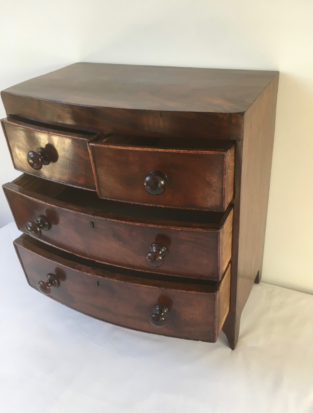 A miniature mahogany bow-fronted chest of drawers featuring turned wooden knobs and a polished grain finish. View IV