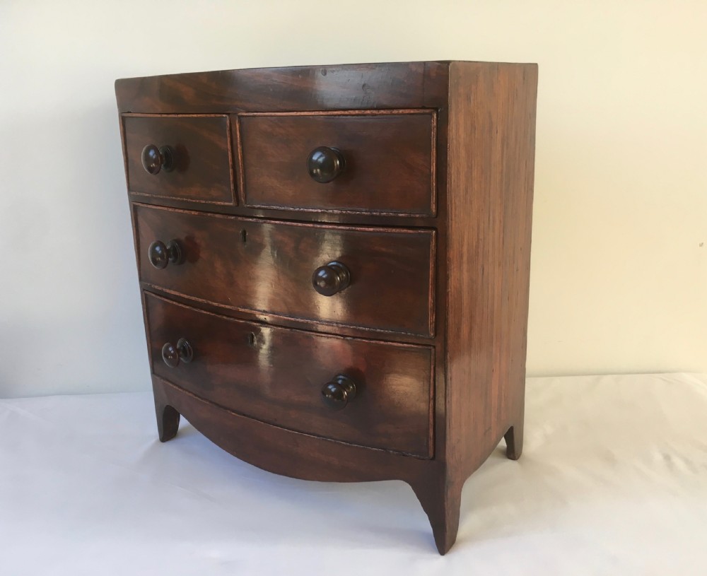 A miniature mahogany bow-fronted chest of drawers featuring turned wooden knobs and a polished grain finish. View V