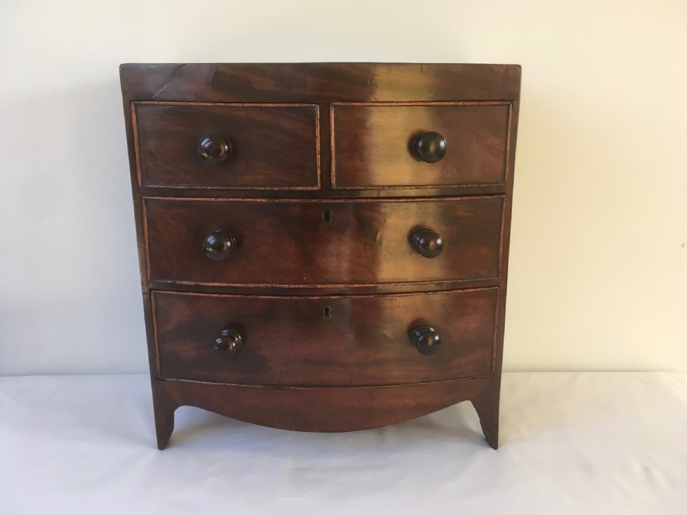 A miniature mahogany bow-fronted chest of drawers featuring turned wooden knobs and a polished grain finish. View VI