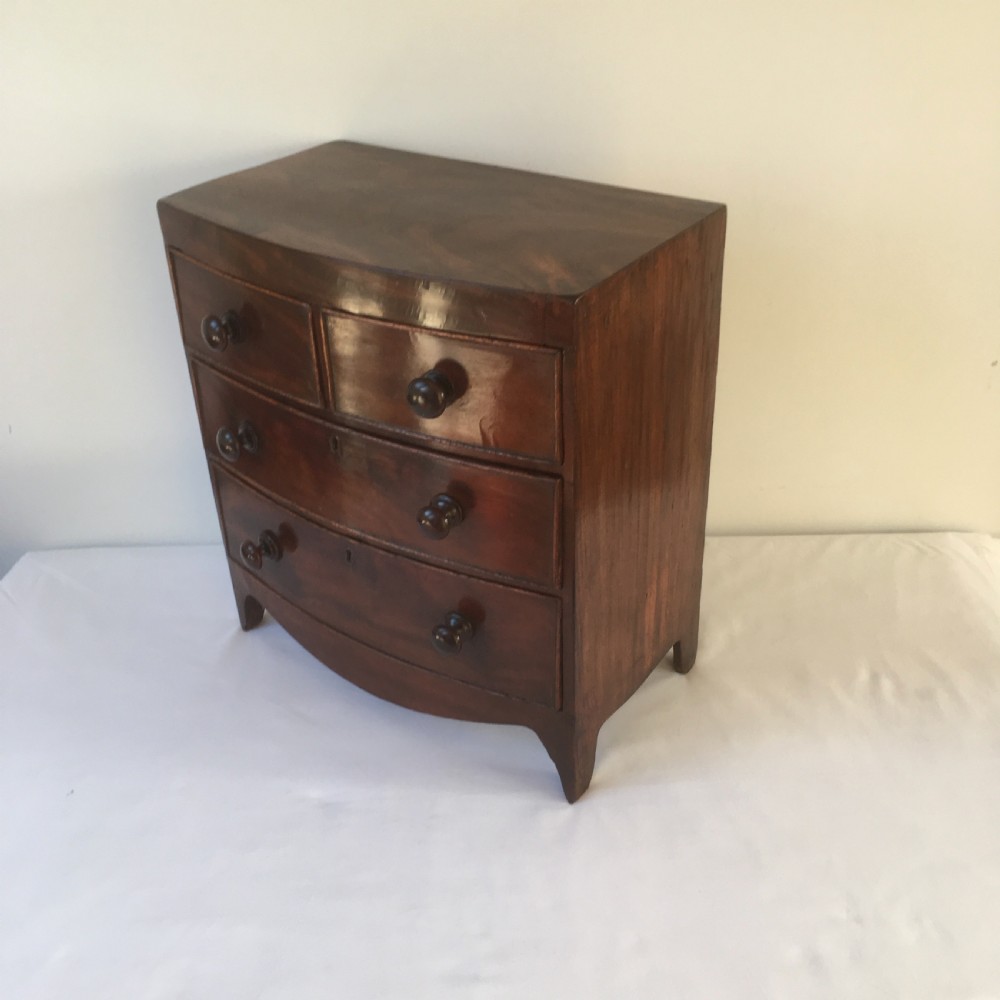 A miniature mahogany bow-fronted chest of drawers featuring turned wooden knobs and a polished grain finish. View VII