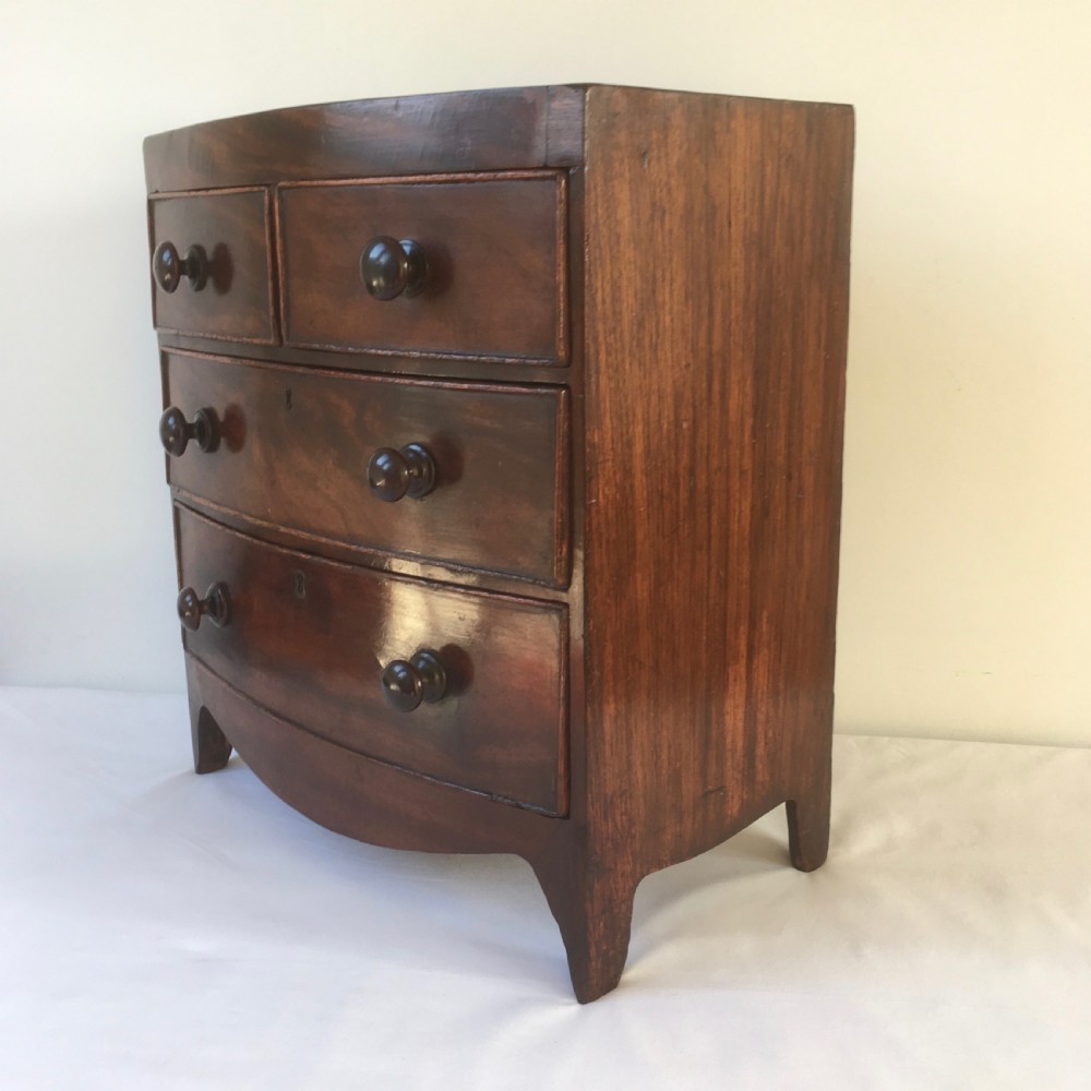 A miniature mahogany bow-fronted chest of drawers featuring turned wooden knobs and a polished grain finish. View VIII