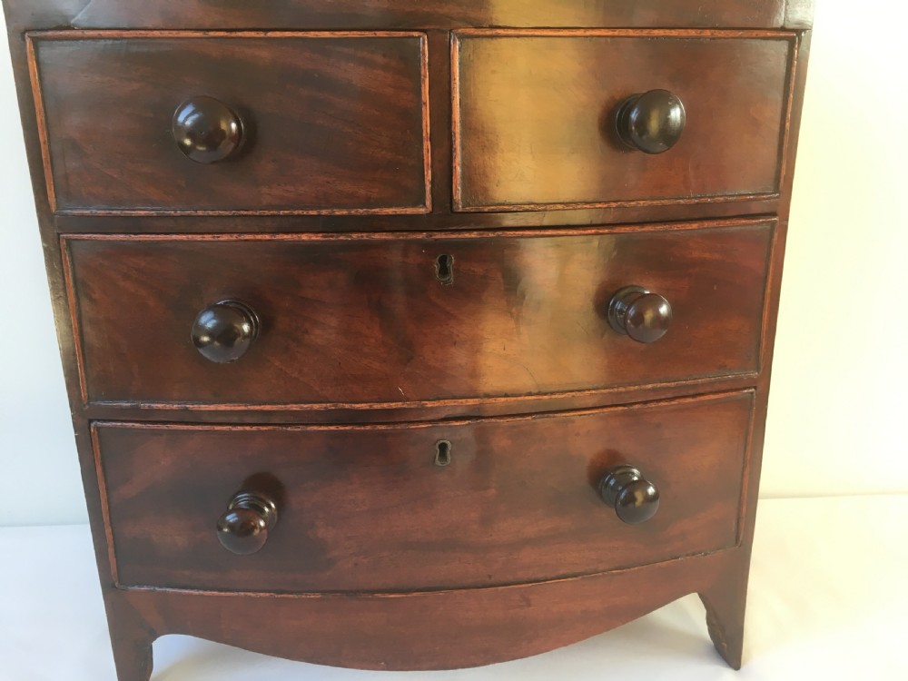 A miniature mahogany bow-fronted chest of drawers featuring turned wooden knobs and a polished grain finish. View X