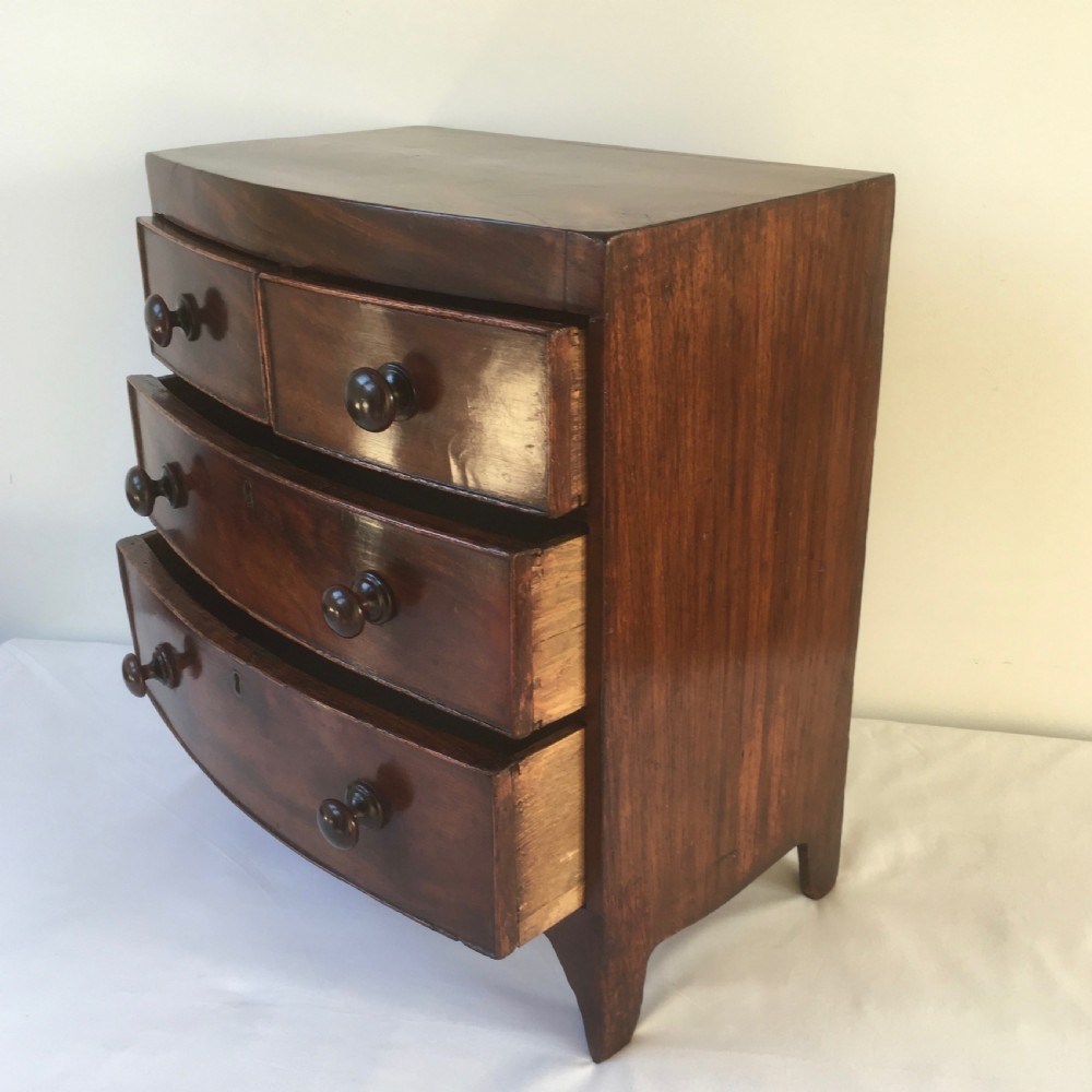 A miniature mahogany bow-fronted chest of drawers featuring turned wooden knobs and a polished grain finish. View XI