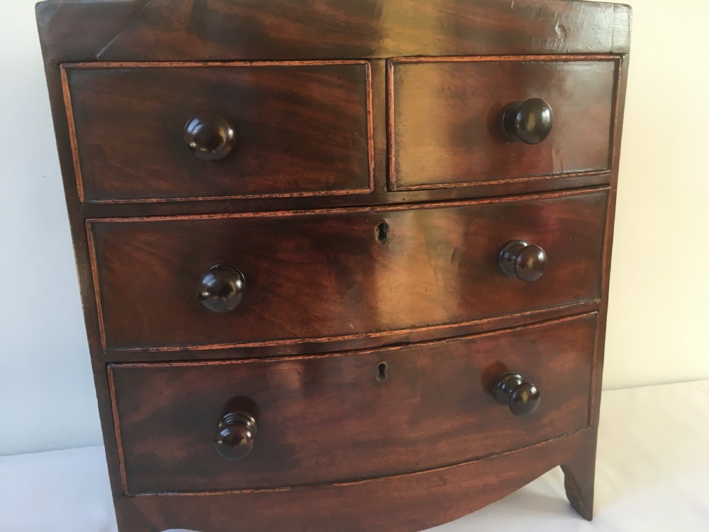 A miniature mahogany bow-fronted chest of drawers featuring turned wooden knobs and a polished grain finish. View XII