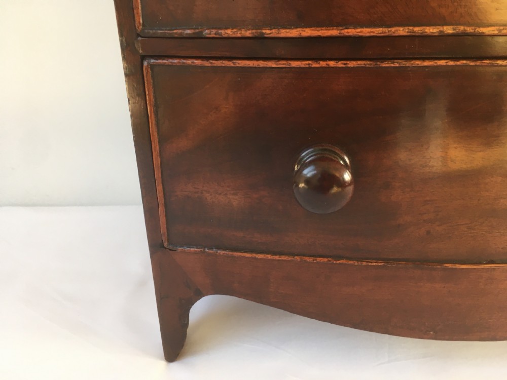 A miniature mahogany bow-fronted chest of drawers featuring turned wooden knobs and a polished grain finish. View XV