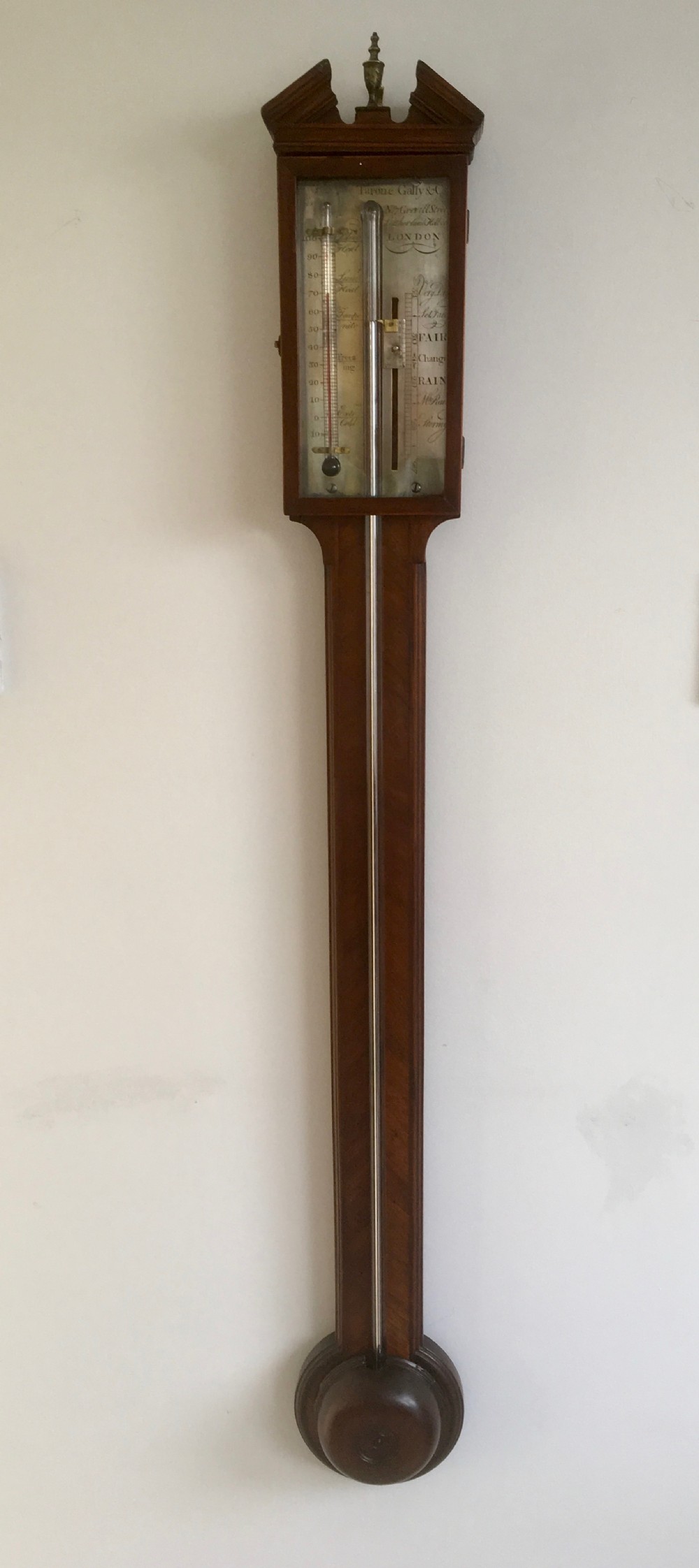 An antique Georgian mahogany stick barometer with a broken arch pediment, central glass tube, silvered register plate, and turned cistern cover.