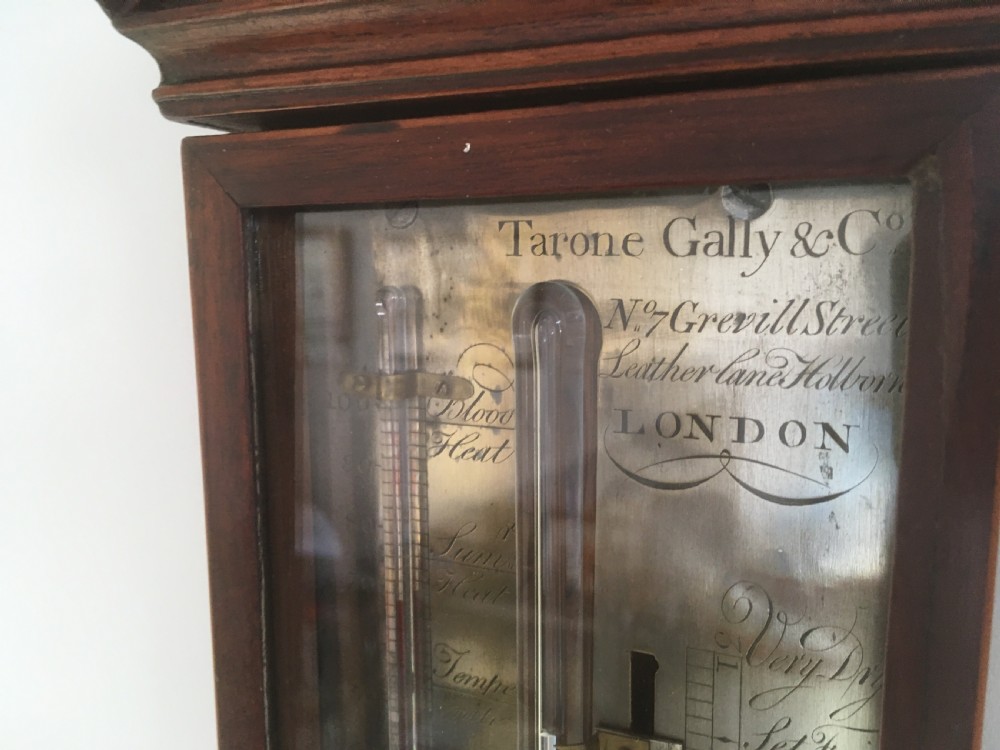 An antique Georgian mahogany stick barometer with a broken arch pediment, central glass tube, silvered register plate, and turned cistern cover. View II