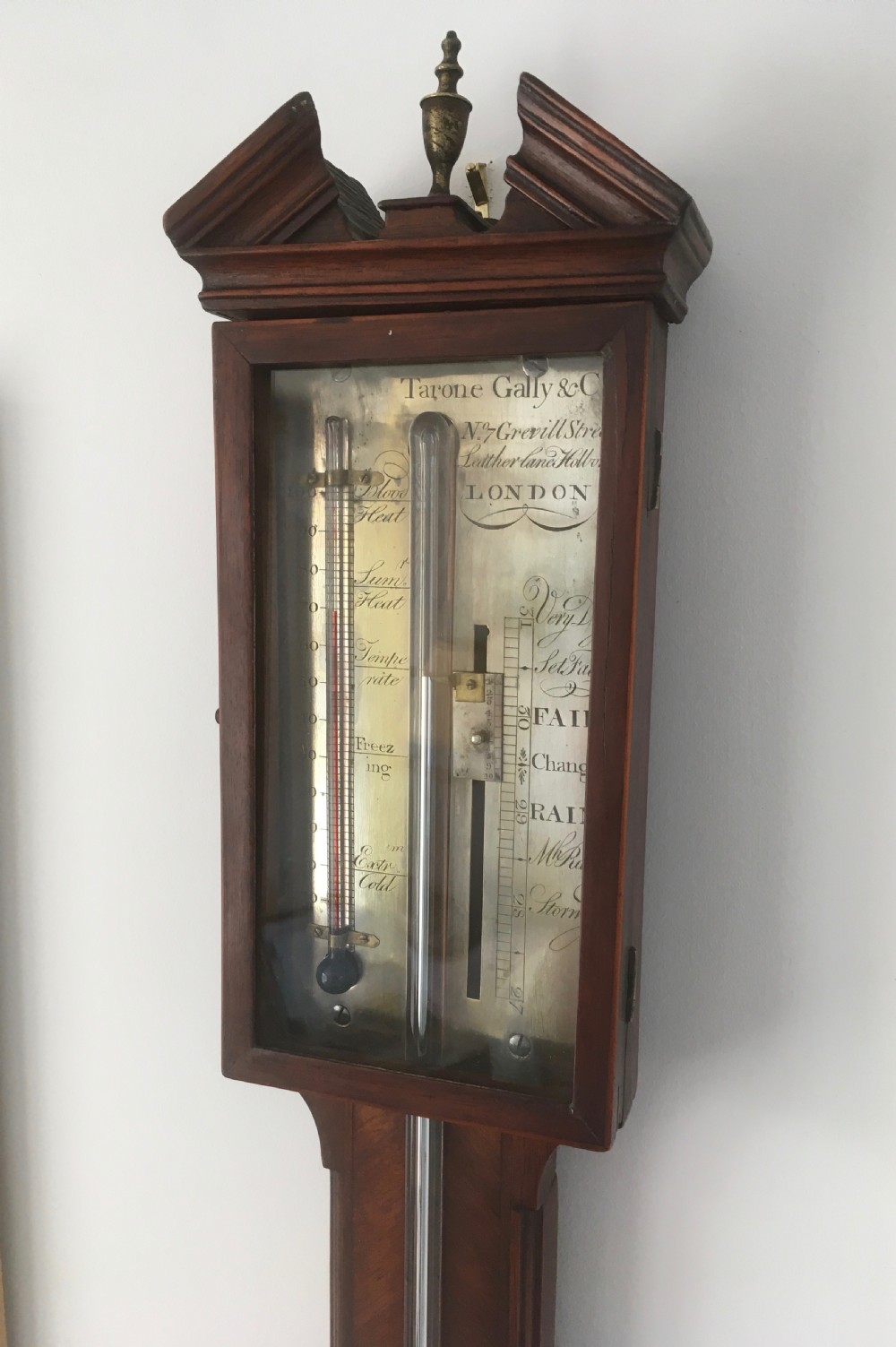An antique Georgian mahogany stick barometer with a broken arch pediment, central glass tube, silvered register plate, and turned cistern cover. View III