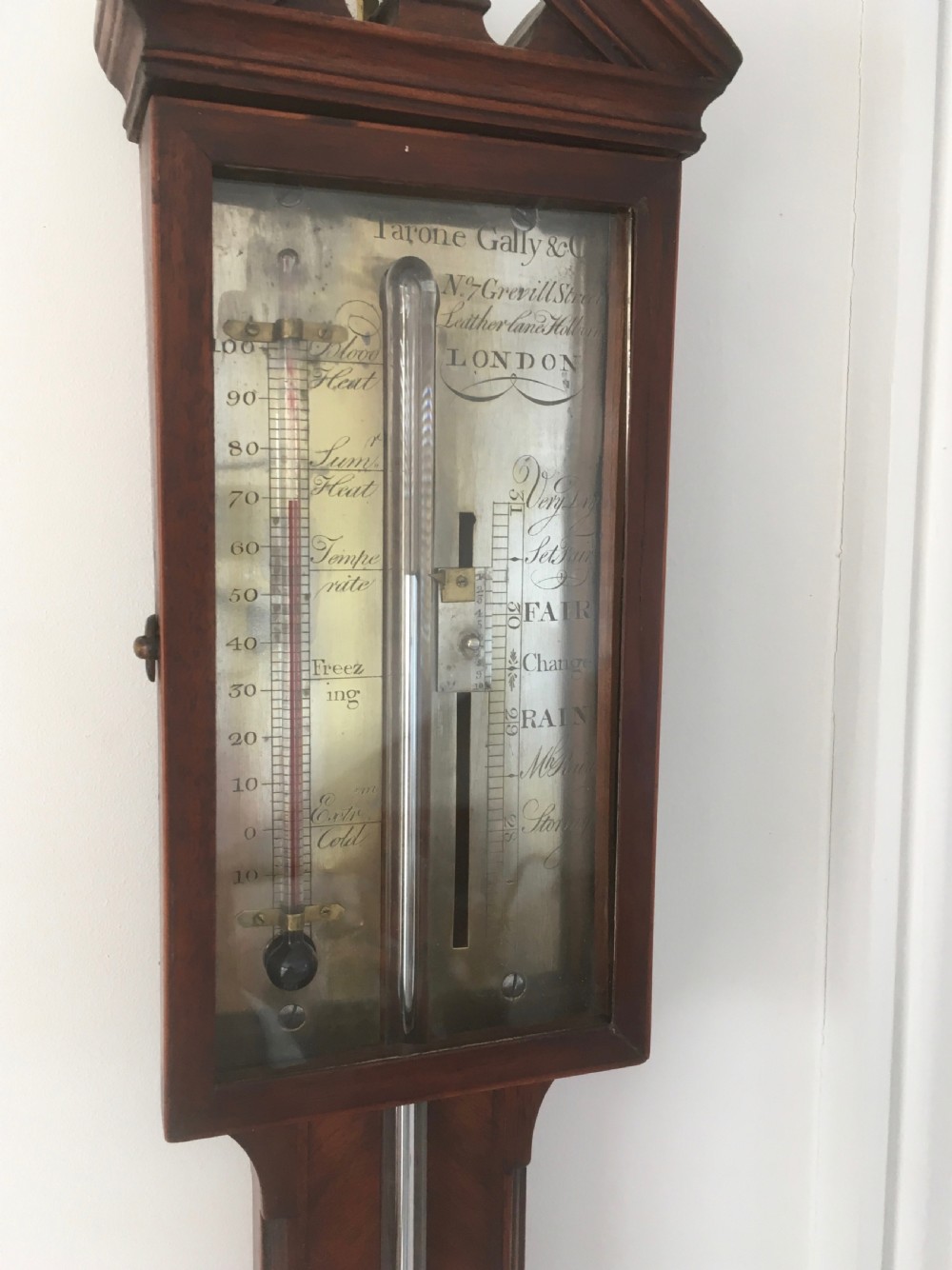 An antique Georgian mahogany stick barometer with a broken arch pediment, central glass tube, silvered register plate, and turned cistern cover. View IV