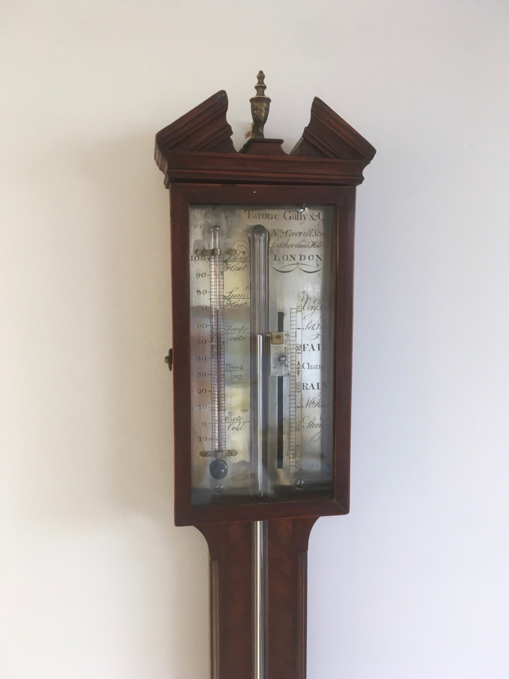 An antique Georgian mahogany stick barometer with a broken arch pediment, central glass tube, silvered register plate, and turned cistern cover. View VII