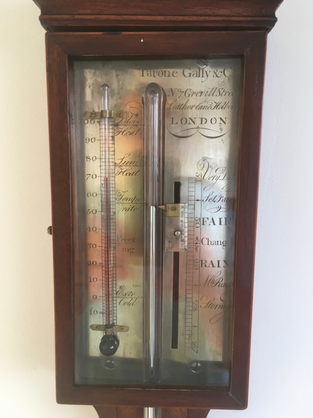 An antique Georgian mahogany stick barometer with a broken arch pediment, central glass tube, silvered register plate, and turned cistern cover. View IX