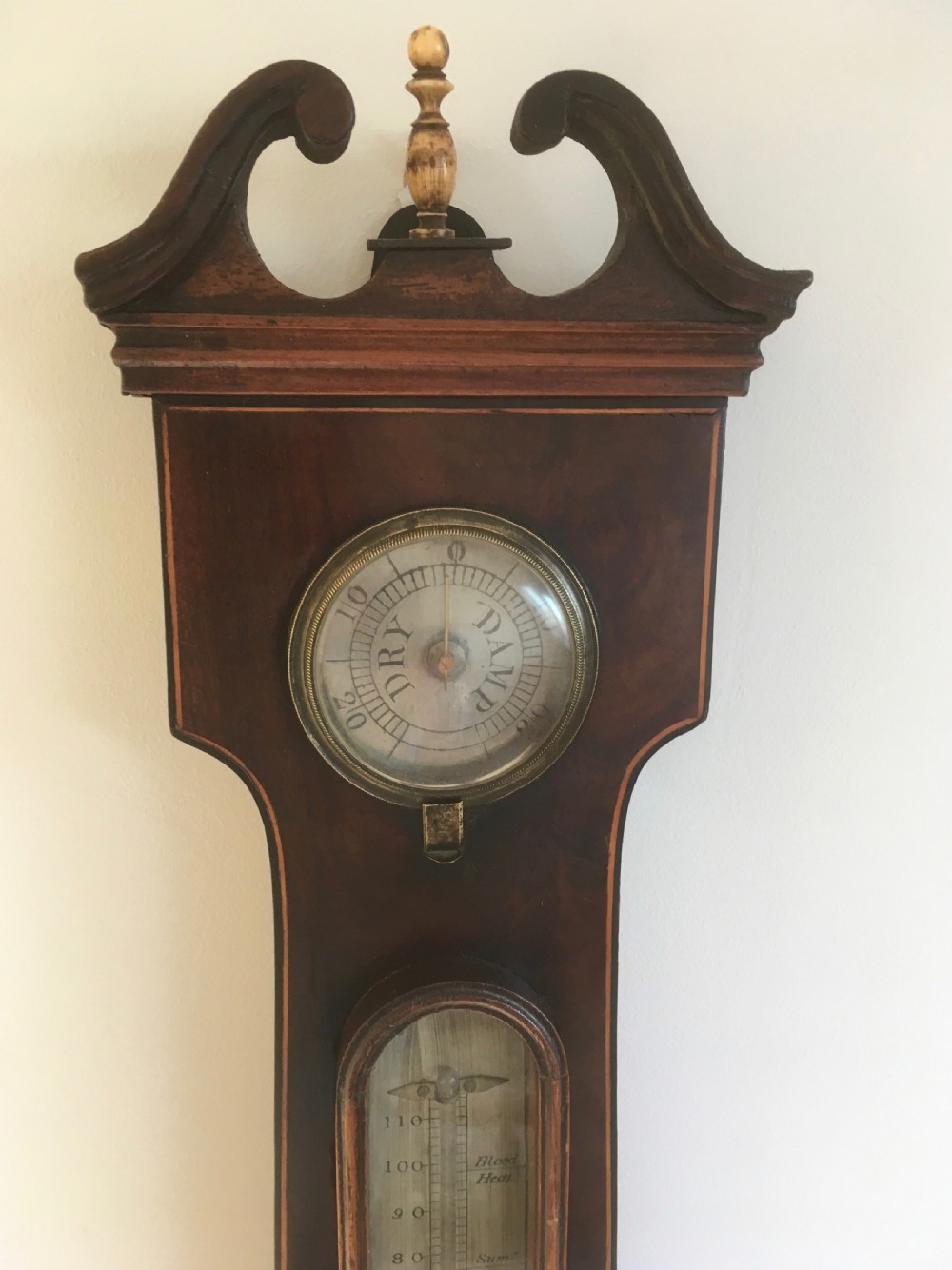 An antique mahogany banjo wheel barometer featuring a top brass finial, thermometer display, central convex mirror, and silvered register dial. View II