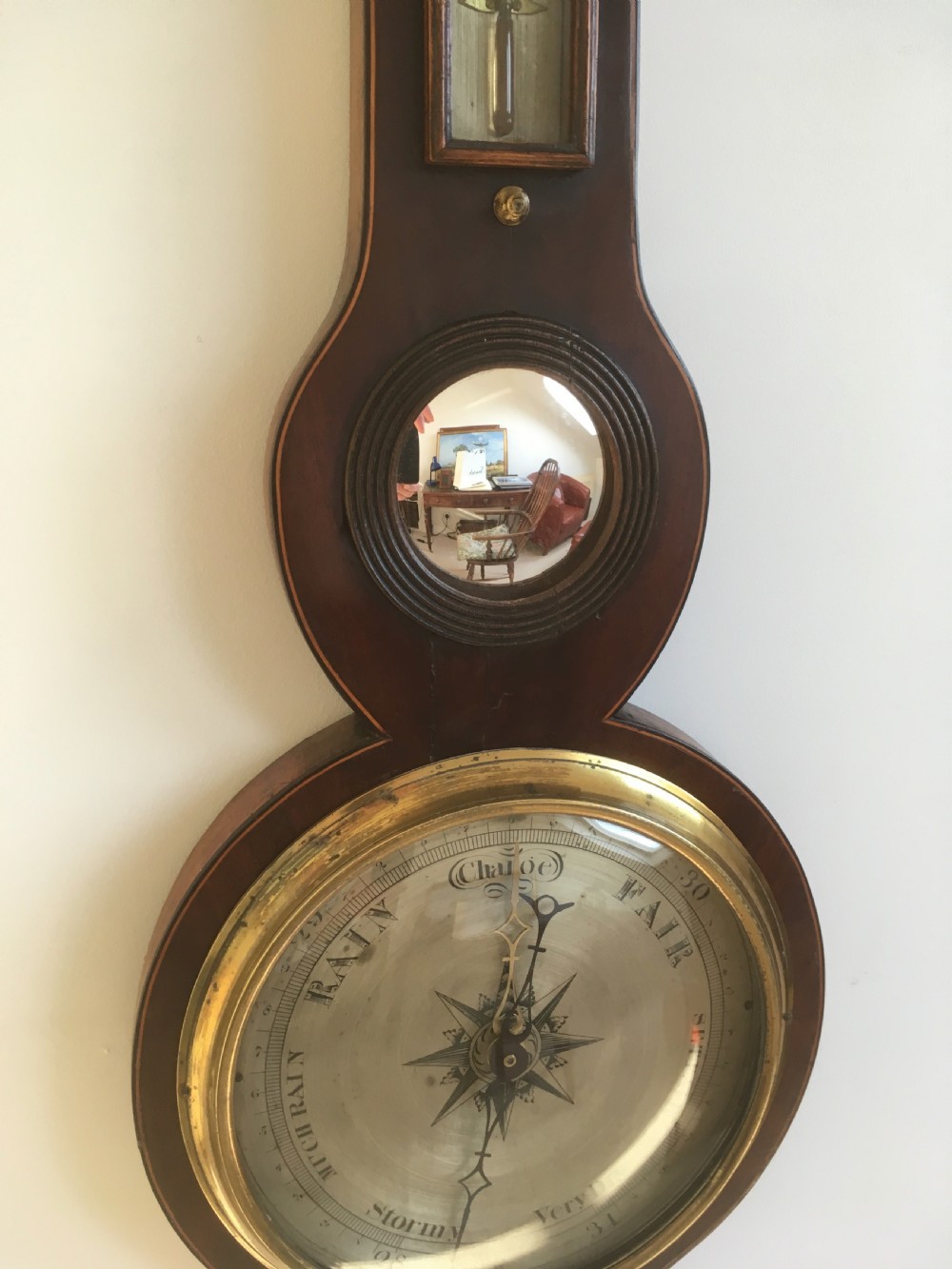 An antique mahogany banjo wheel barometer featuring a top brass finial, thermometer display, central convex mirror, and silvered register dial. View IV