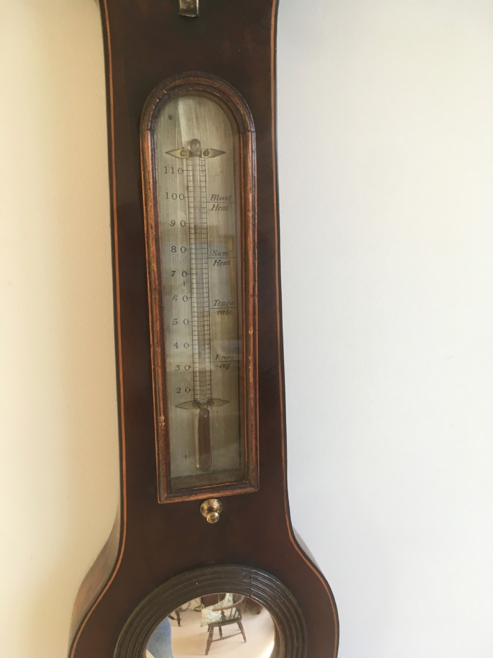 An antique mahogany banjo wheel barometer featuring a top brass finial, thermometer display, central convex mirror, and silvered register dial. View VIII