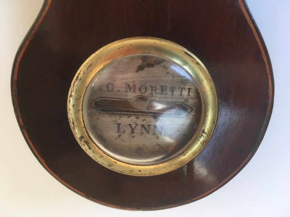 An antique mahogany banjo wheel barometer featuring a top brass finial, thermometer display, central convex mirror, and silvered register dial. View XI