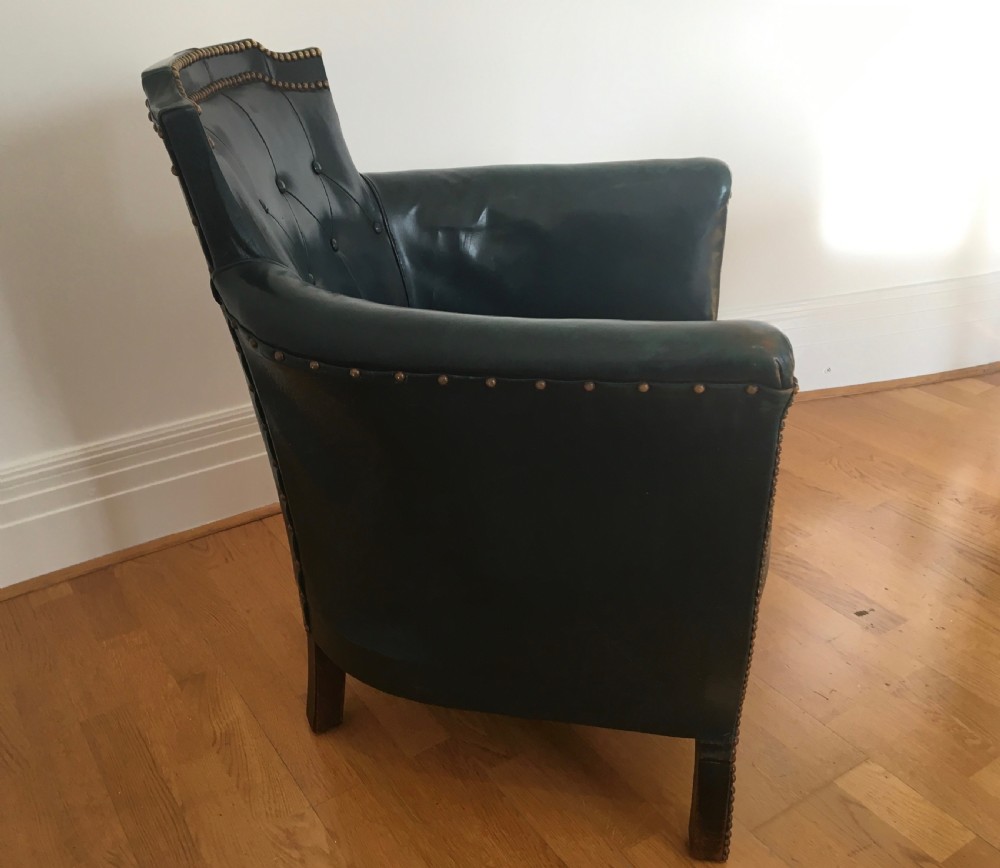 An Edwardian dark green leather library armchair featuring deep button tufting, brass stud trim, and dark timber legs.