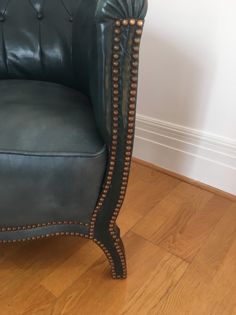 An Edwardian dark green leather library armchair featuring deep button tufting, brass stud trim, and dark timber legs. View V