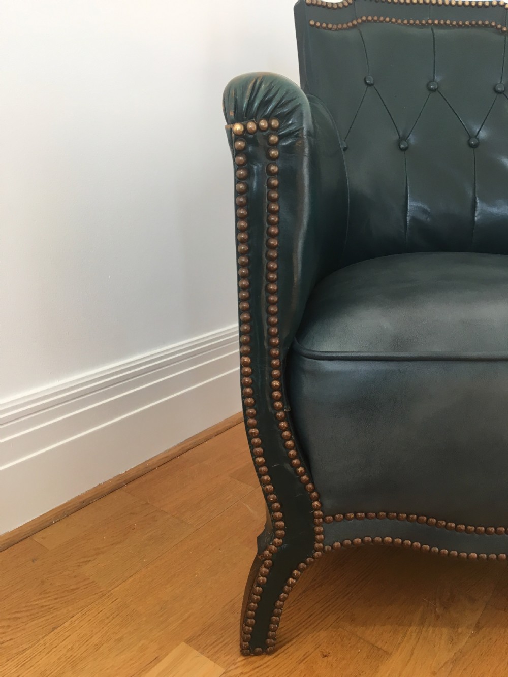 An Edwardian dark green leather library armchair featuring deep button tufting, brass stud trim, and dark timber legs. View IX