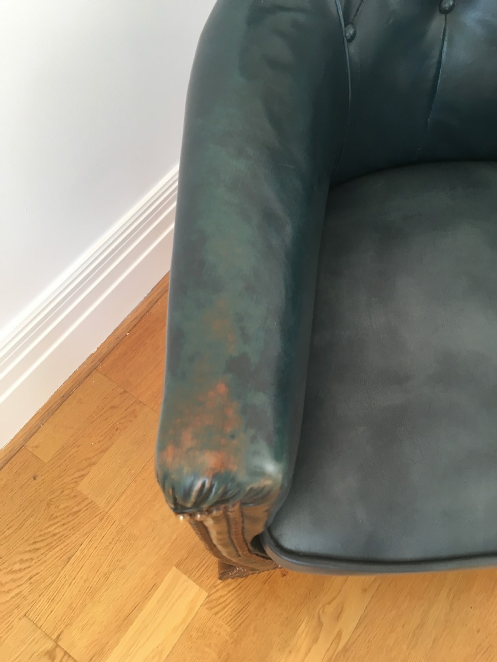 An Edwardian dark green leather library armchair featuring deep button tufting, brass stud trim, and dark timber legs. View X