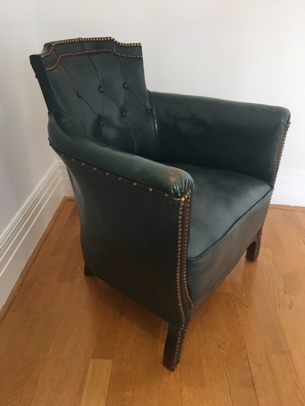 An Edwardian dark green leather library armchair featuring deep button tufting, brass stud trim, and dark timber legs. View XV
