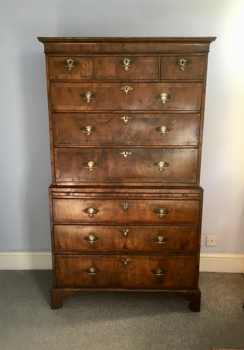An 18th-century George II walnut tallboy chest-on-chest featuring figured veneer drawers, brass drop handles, and bracket feet.