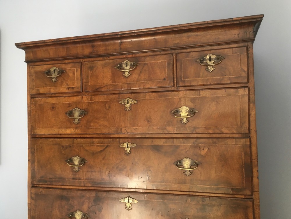An 18th-century George II walnut tallboy chest-on-chest featuring figured veneer drawers, brass drop handles, and bracket feet. View V