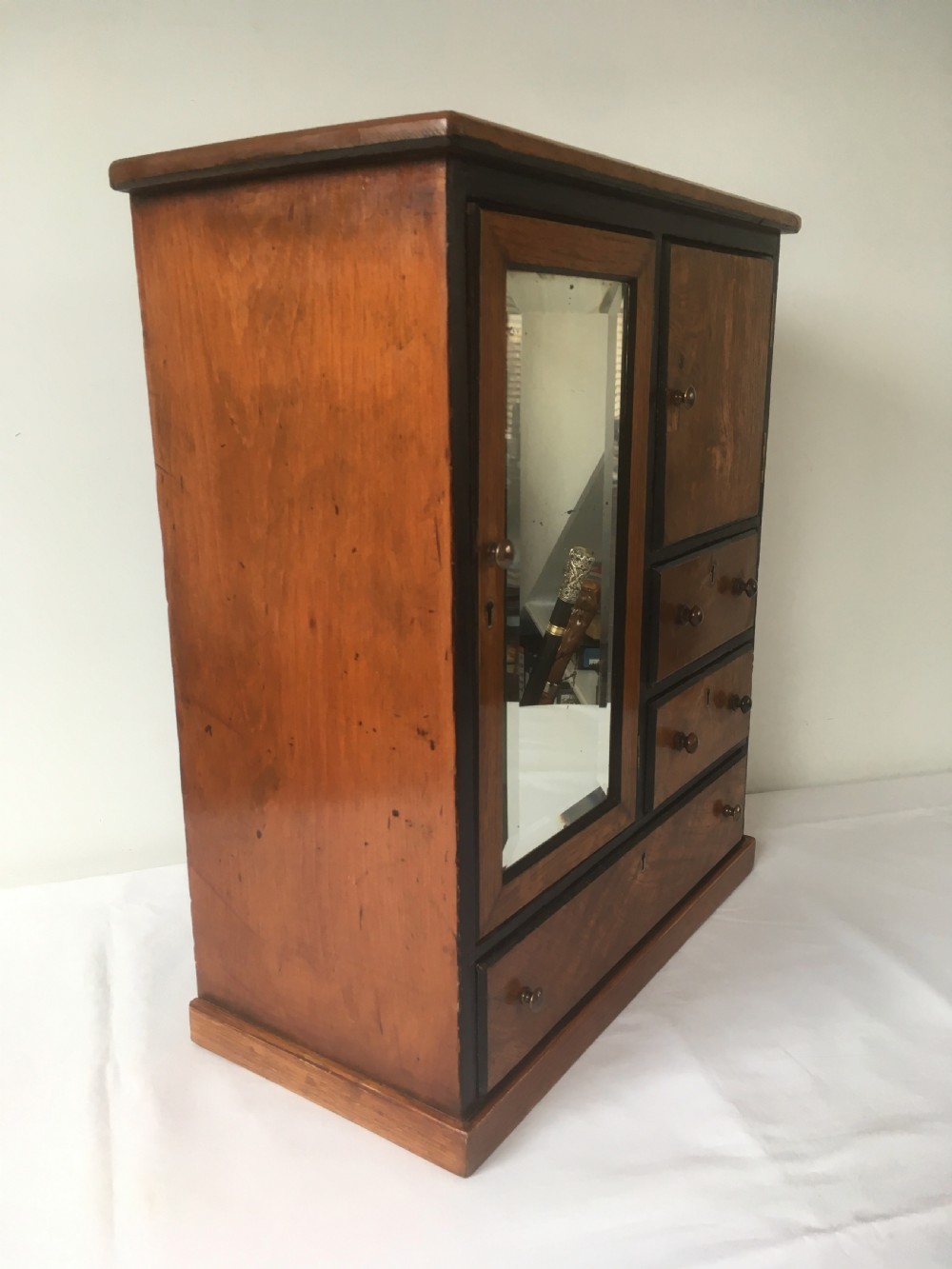 A miniature oak compactum wardrobe featuring a left door with a rectangular mirror, a right cupboard door, three small drawers, wooden knob handles, and dark ebonised framing. View IV
