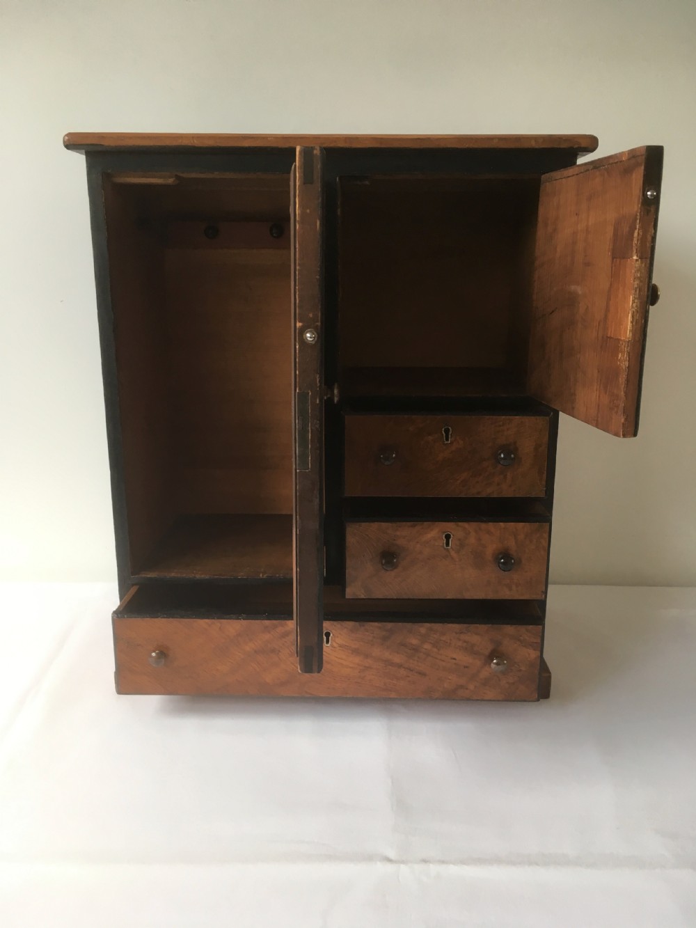 A miniature oak compactum wardrobe featuring a left door with a rectangular mirror, a right cupboard door, three small drawers, wooden knob handles, and dark ebonised framing. View V