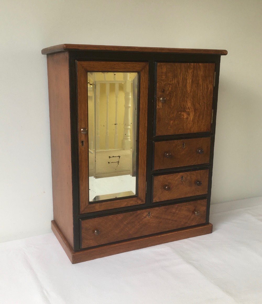 A miniature oak compactum wardrobe featuring a left door with a rectangular mirror, a right cupboard door, three small drawers, wooden knob handles, and dark ebonised framing. View VI