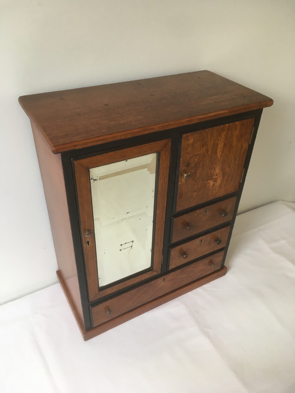 A miniature oak compactum wardrobe featuring a left door with a rectangular mirror, a right cupboard door, three small drawers, wooden knob handles, and dark ebonised framing. View VIII