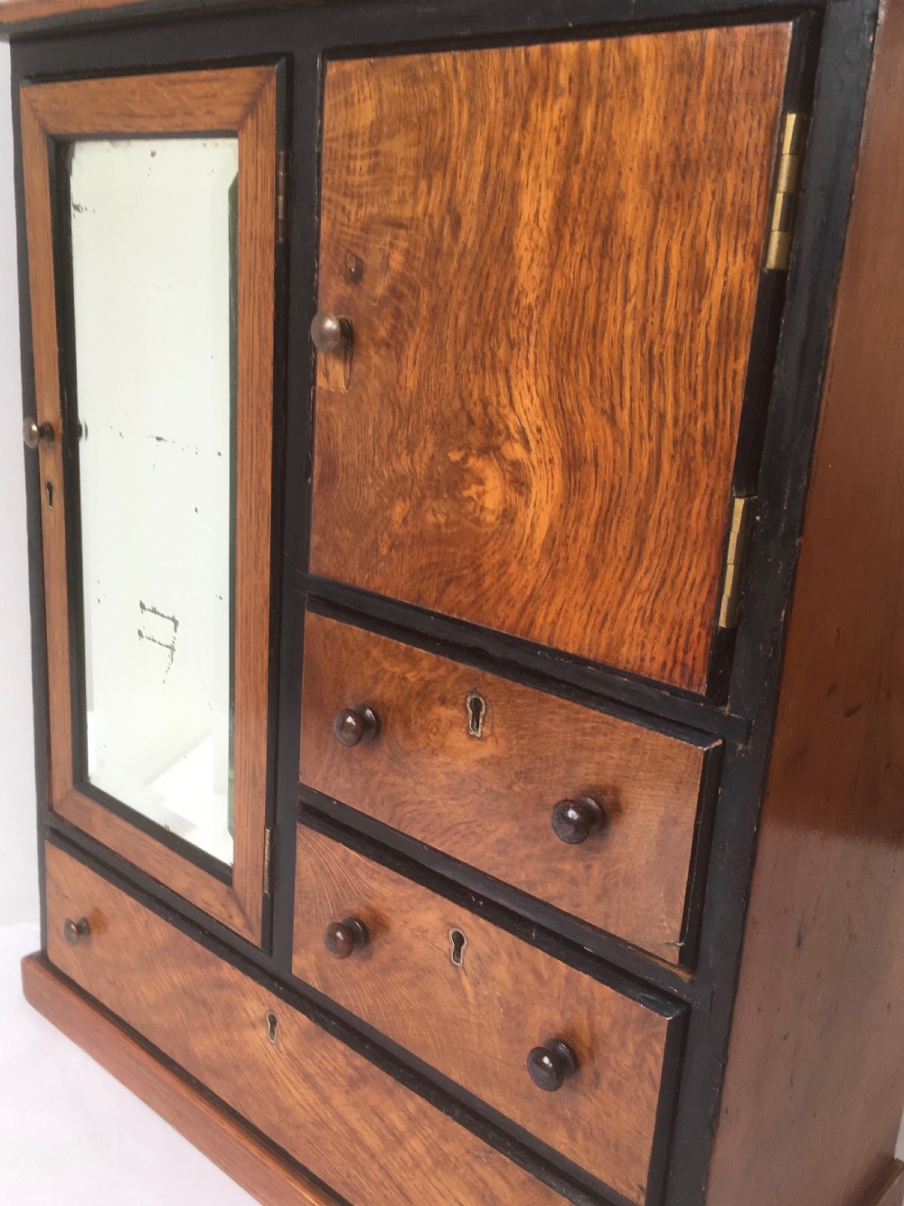 A miniature oak compactum wardrobe featuring a left door with a rectangular mirror, a right cupboard door, three small drawers, wooden knob handles, and dark ebonised framing. View IX