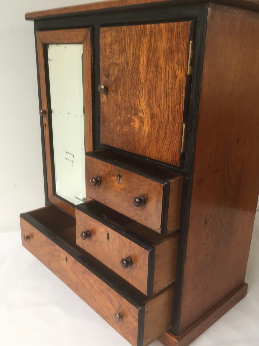 A miniature oak compactum wardrobe featuring a left door with a rectangular mirror, a right cupboard door, three small drawers, wooden knob handles, and dark ebonised framing. View X