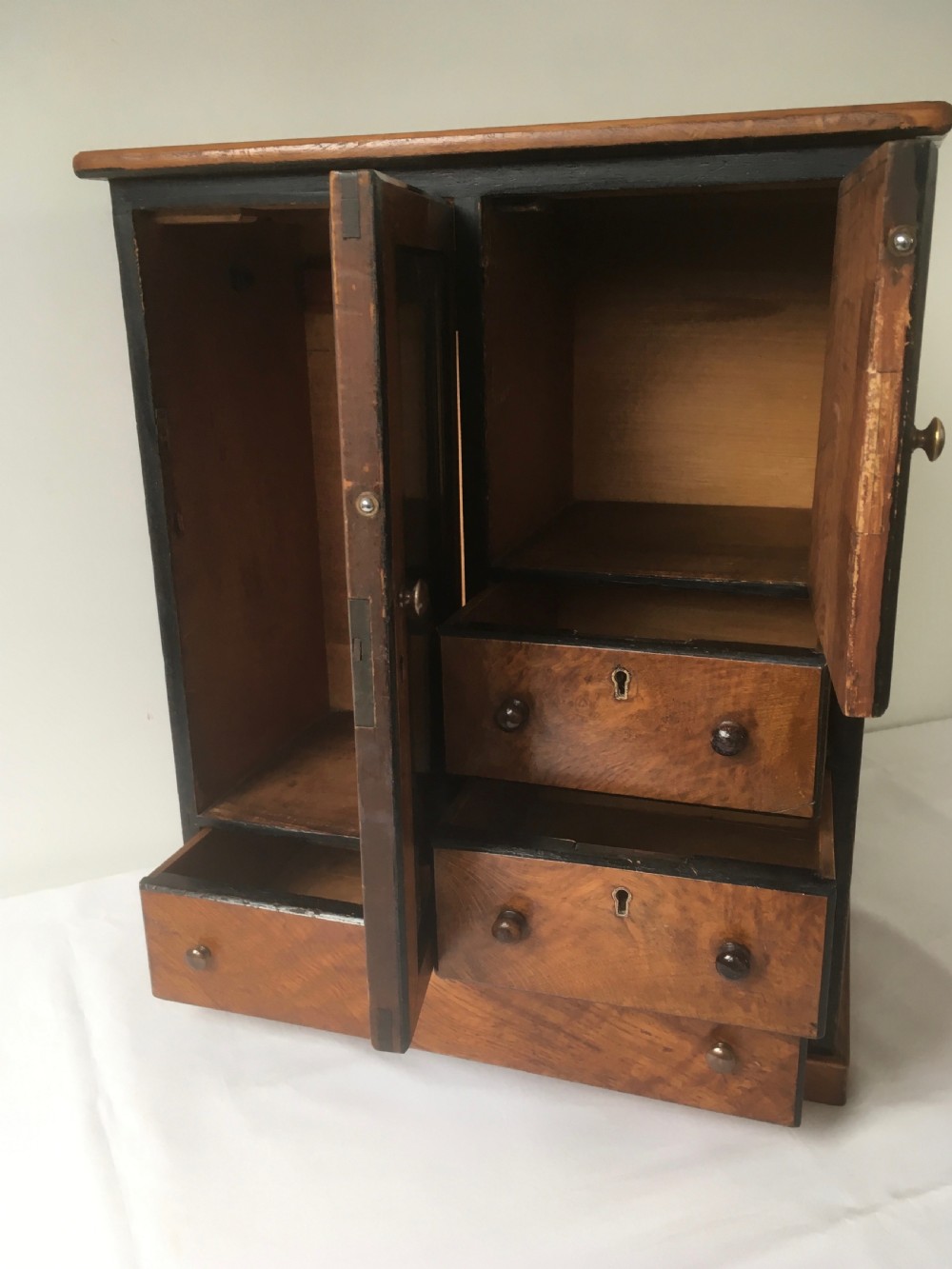 A miniature oak compactum wardrobe featuring a left door with a rectangular mirror, a right cupboard door, three small drawers, wooden knob handles, and dark ebonised framing. View XI
