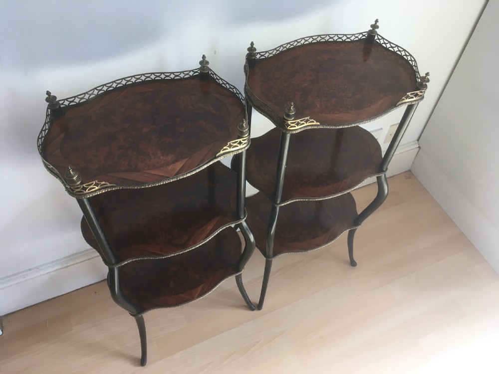 A pair of three-tiered French style side tables crafted from dark wood with inlaid marquetry work, gilt metal gallery rails, and cabriole legs.