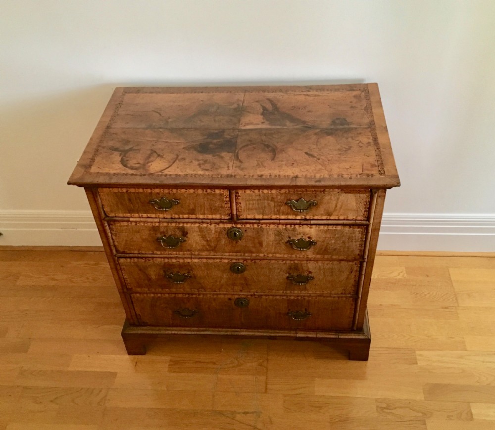 An eighteenth-century walnut chest of drawers featuring decorative poker work inlay, brass swing handles, keyhole escutcheons, and straight bracket feet.